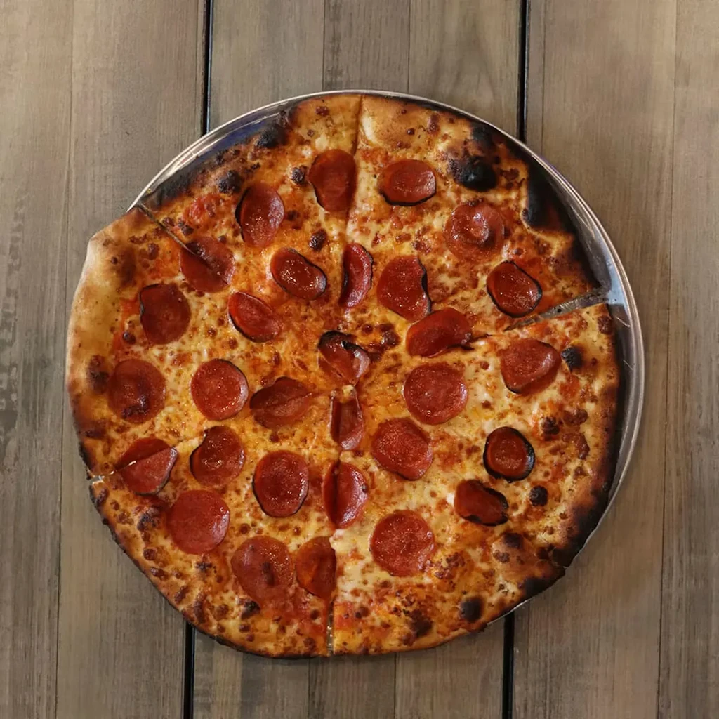 Pre-sliced pepperoni pizza on a silver pan, on a wooden table.