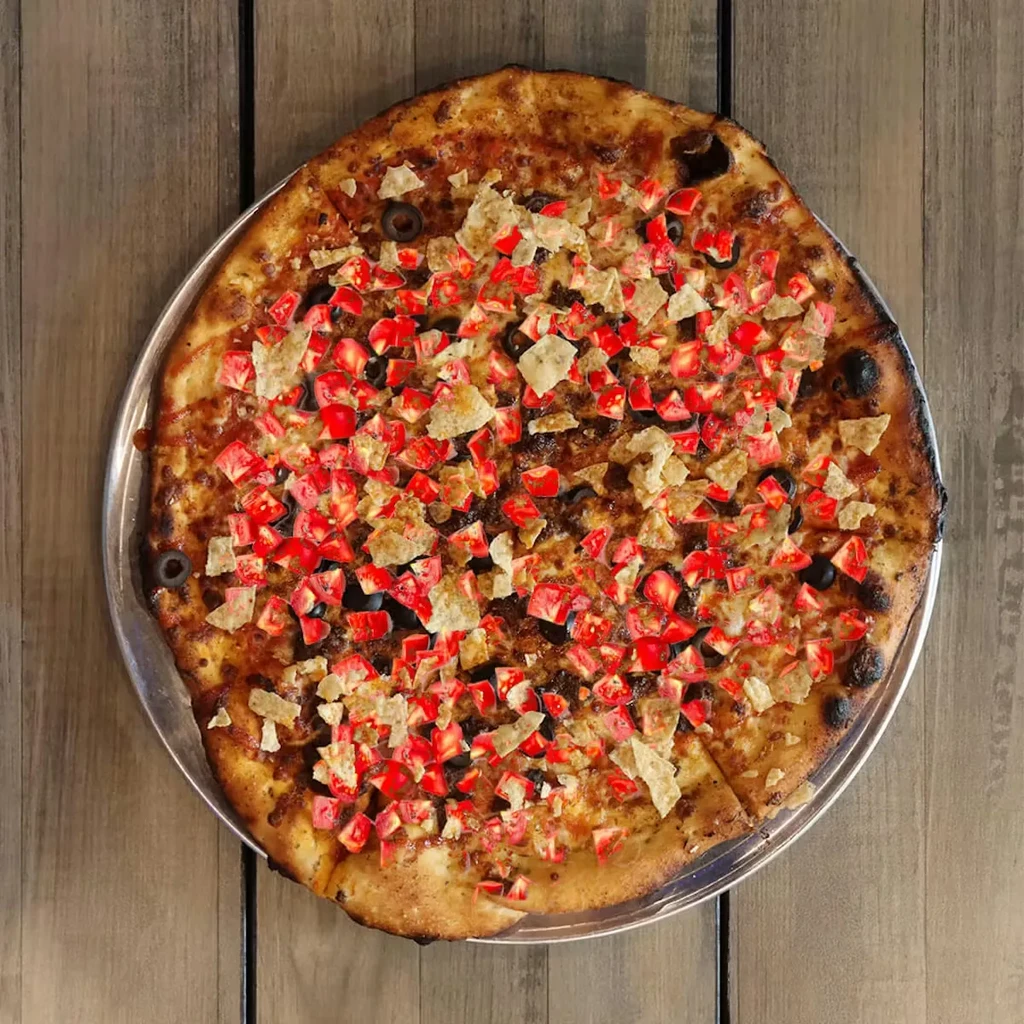 Round pizza with red toppings, olives, and crispy pieces on wood.
