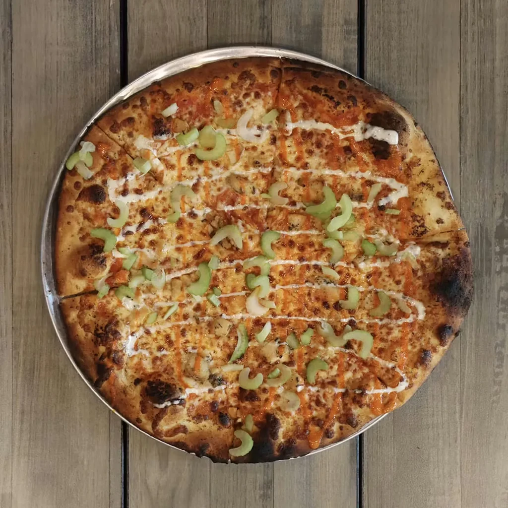 Round buffalo chicken pizza, pre-cut, with celery and white drizzles.
