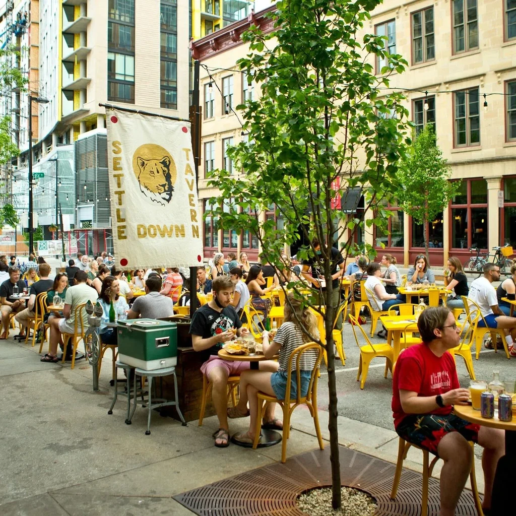 Lively outdoor dining at Settle Down Tavern with yellow tables.