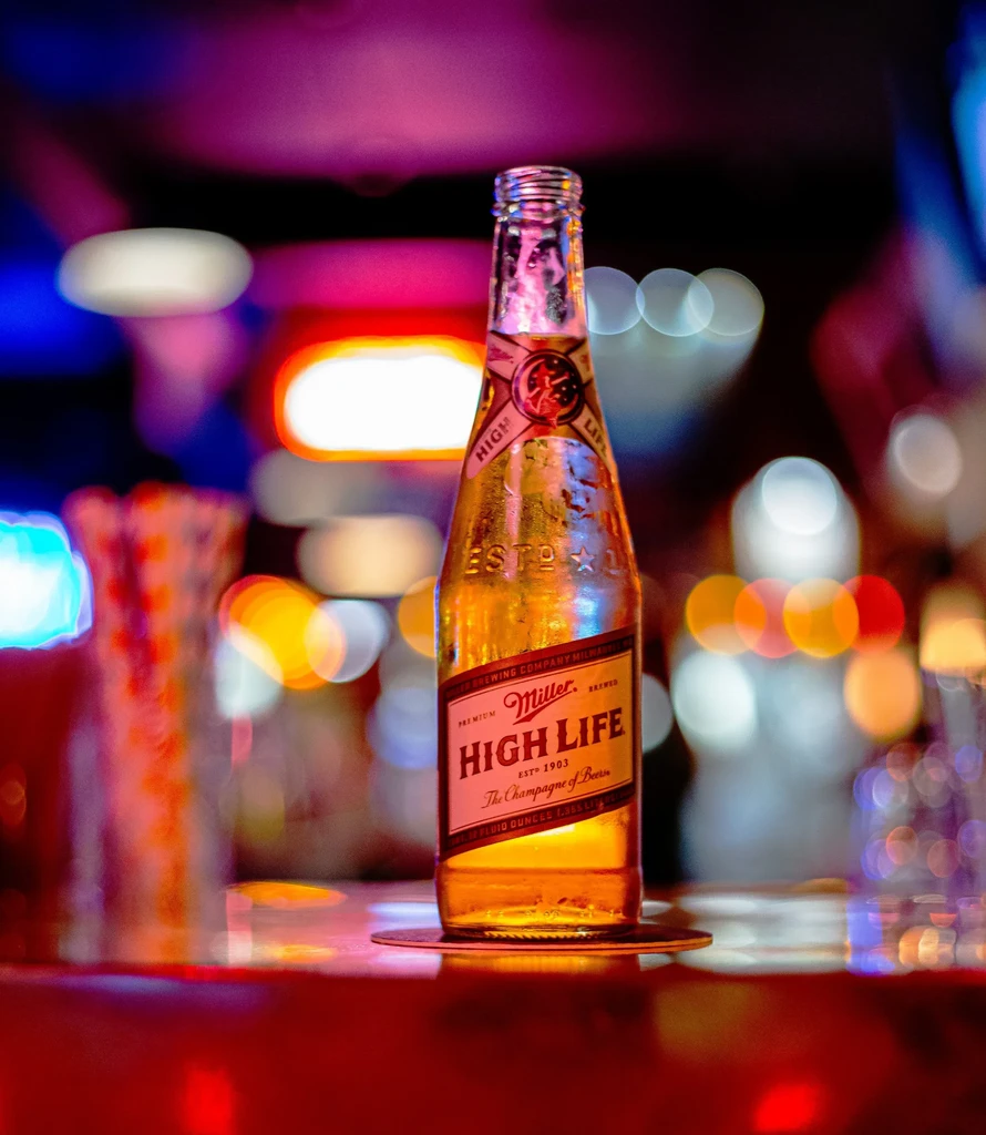 Chilled Miller High Life bottle with condensation against blurred bar lights.