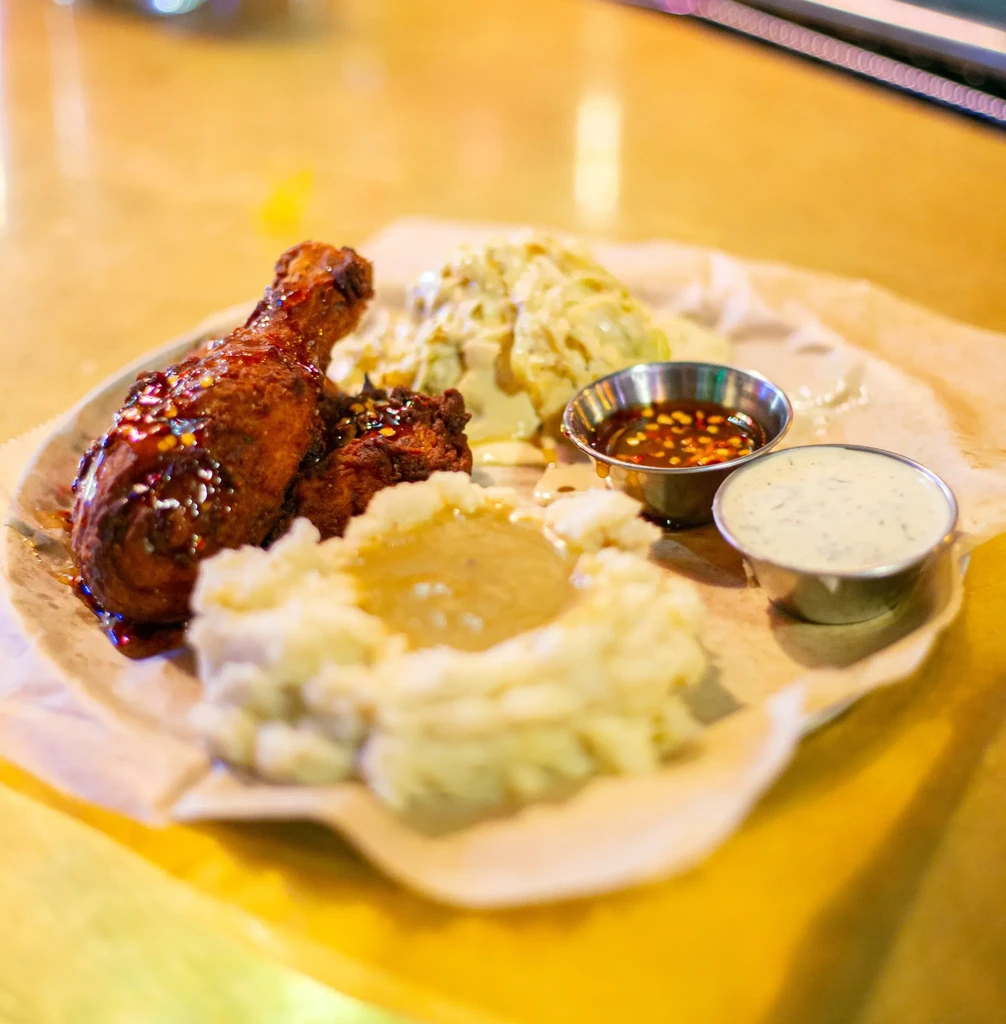 A plate of fried chicken, mashed potatoes, coleslaw, and dipping sauces.