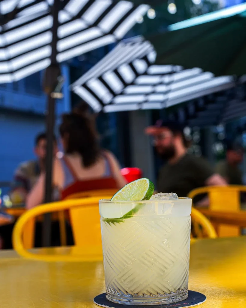 Textured glass cocktail with lime on yellow table, blurred patio background.