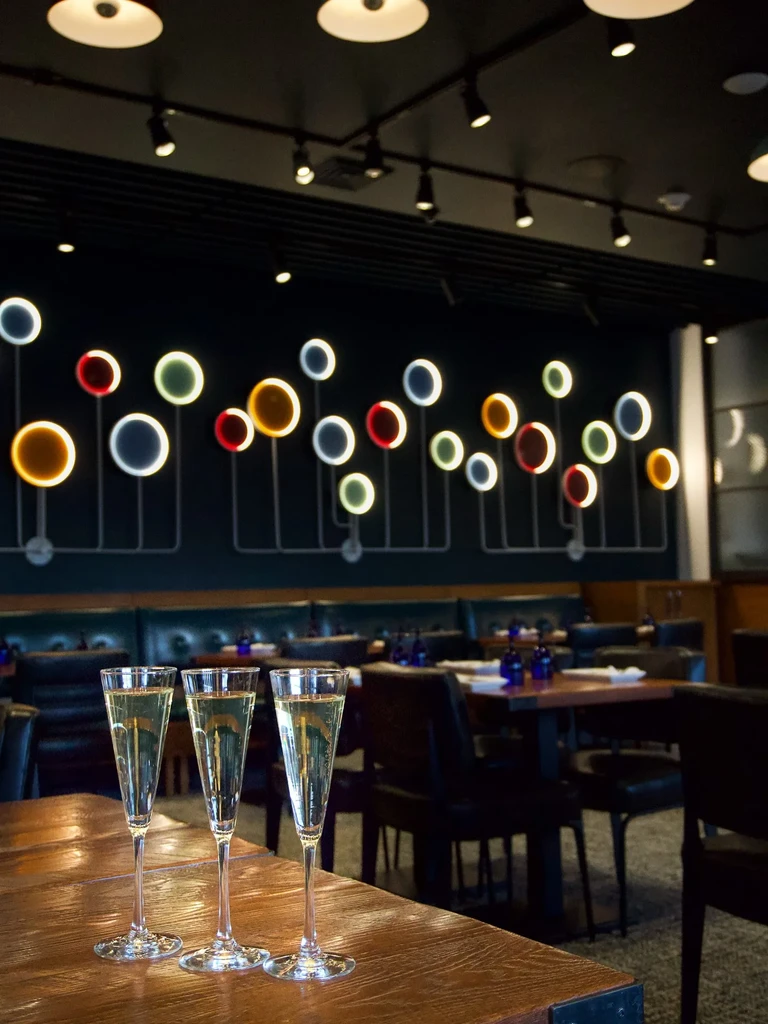 Three sparkling flutes in a modern restaurant with circular light art.