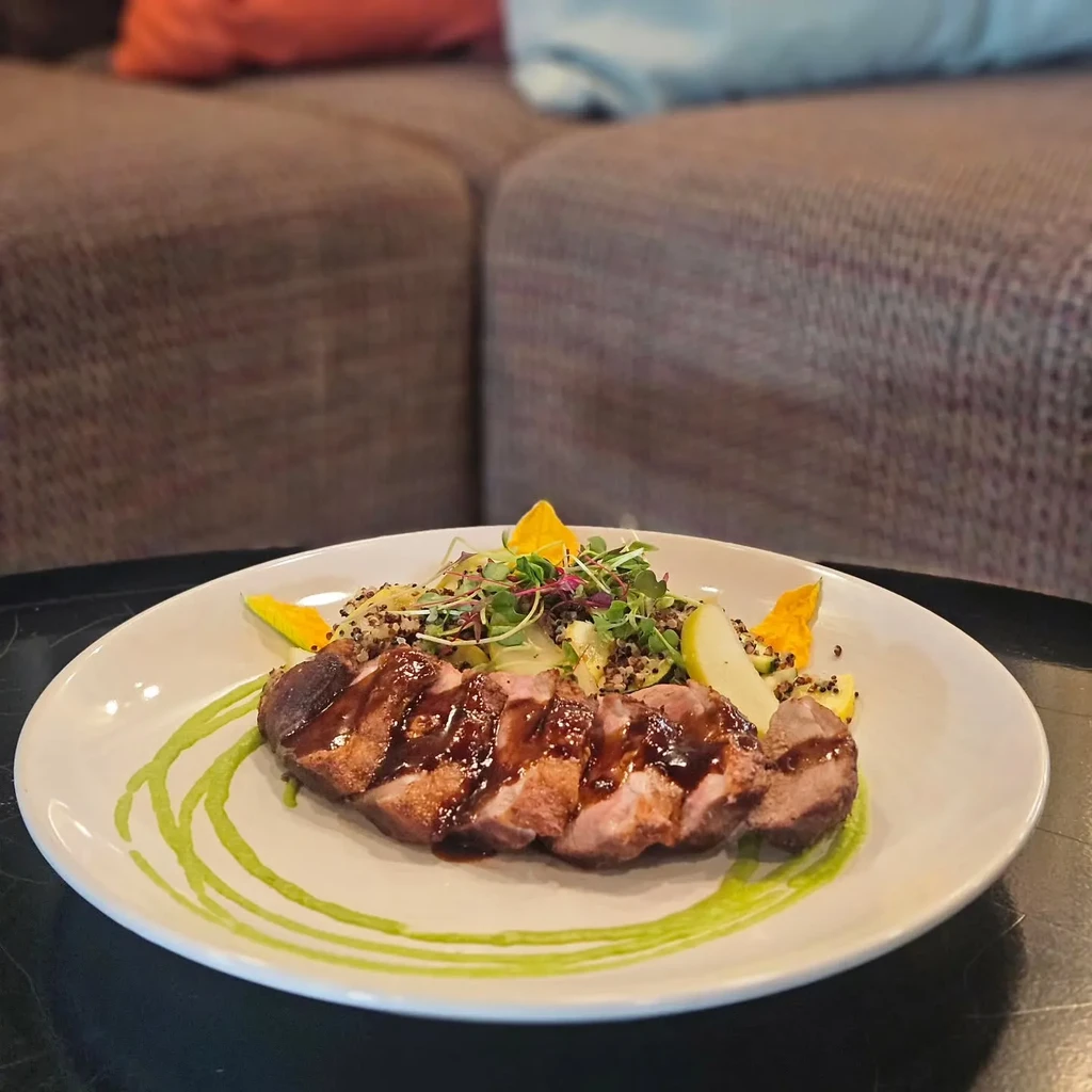 Plated seared meat with colorful salad and fruit in a restaurant setting.