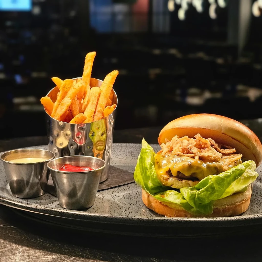 Gourmet open-faced burger, fries, and two sauces on a dark plate.