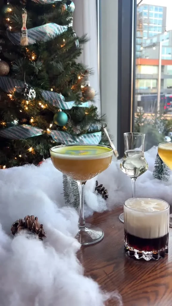Three festive cocktails on a snowy table with a Christmas tree.