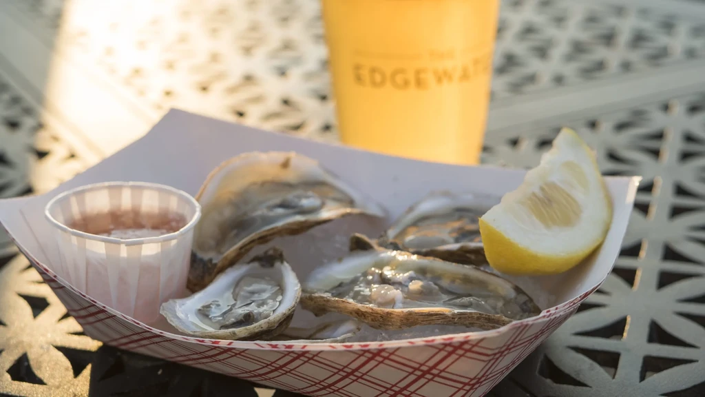 Fresh oysters on ice with lemon wedge and sauce outdoors.