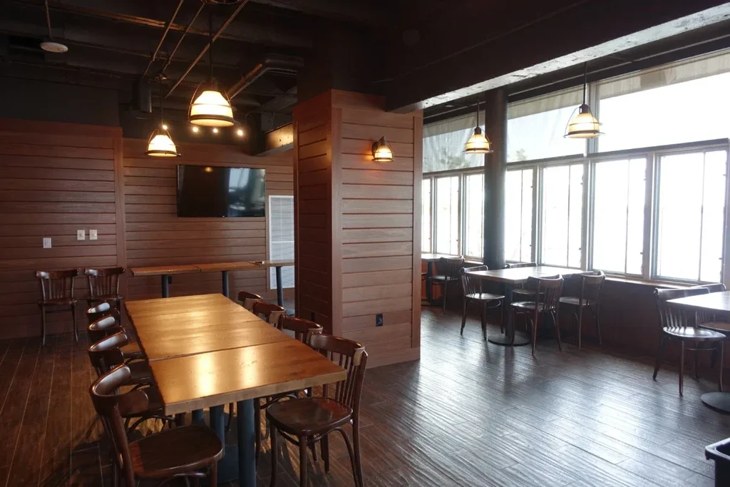 Empty modern-rustic restaurant interior with communal table and large windows.
