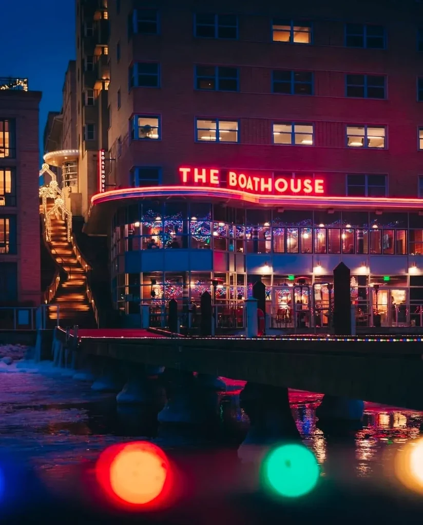 Nighttime view of THE BOATHOUSE restaurant by water with colorful lights.