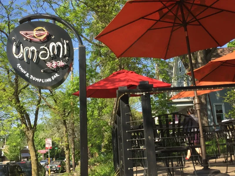 Restaurant exterior: Umami Ramen sign, orange patio umbrellas, and green trees.