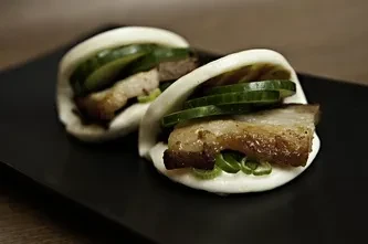 Two gua bao with braised pork belly, cucumber, and herbs.