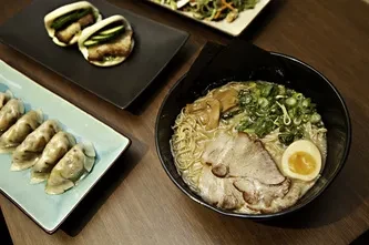 Top-down view of ramen, gyoza, and bao buns on a wooden table.