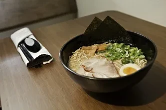 Close-up of black ramen bowl with chashu, egg, nori, green onions.