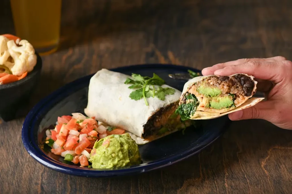 Hand holding a burrito cross-section, with guacamole and pico de gallo.