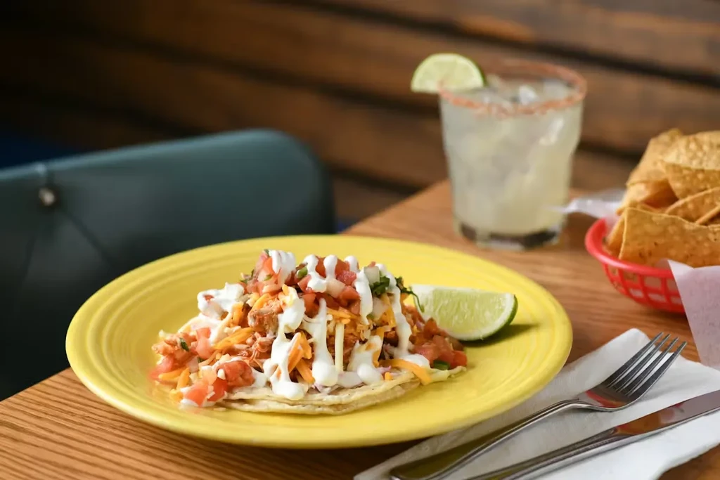 Two tacos with cheese, pico, sour cream, margarita, and chips.