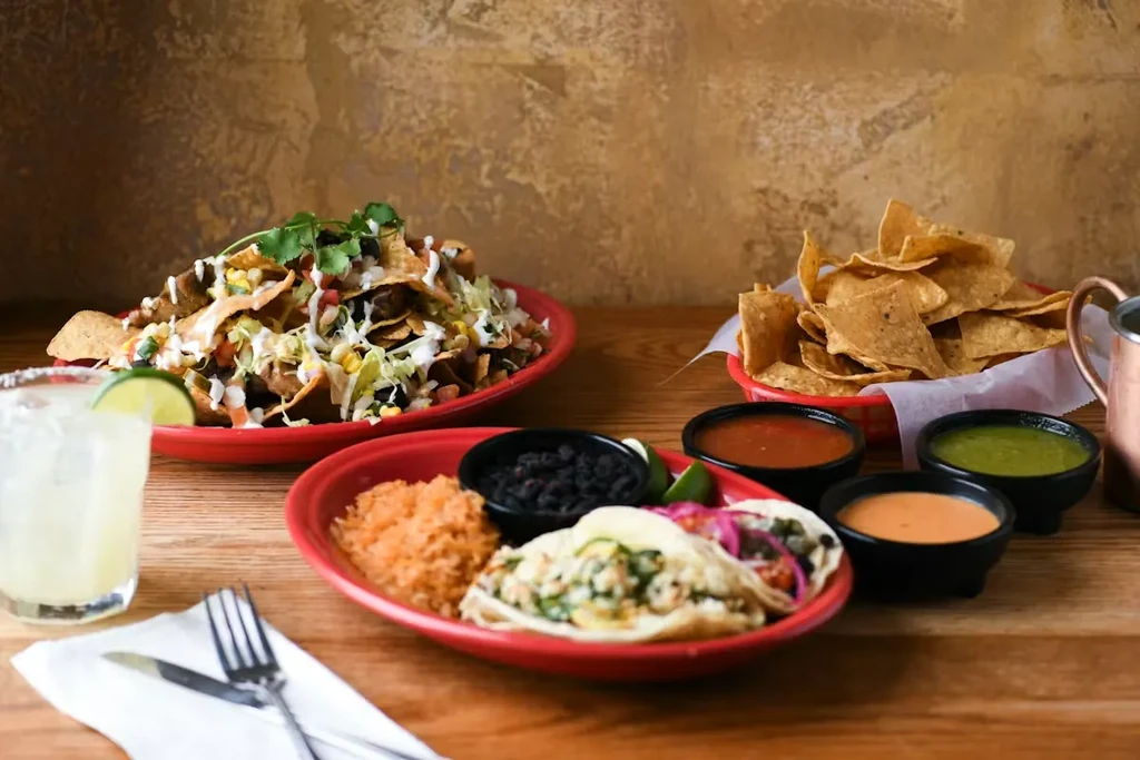 Nachos, tacos, rice, beans, and salsas on a rustic table.