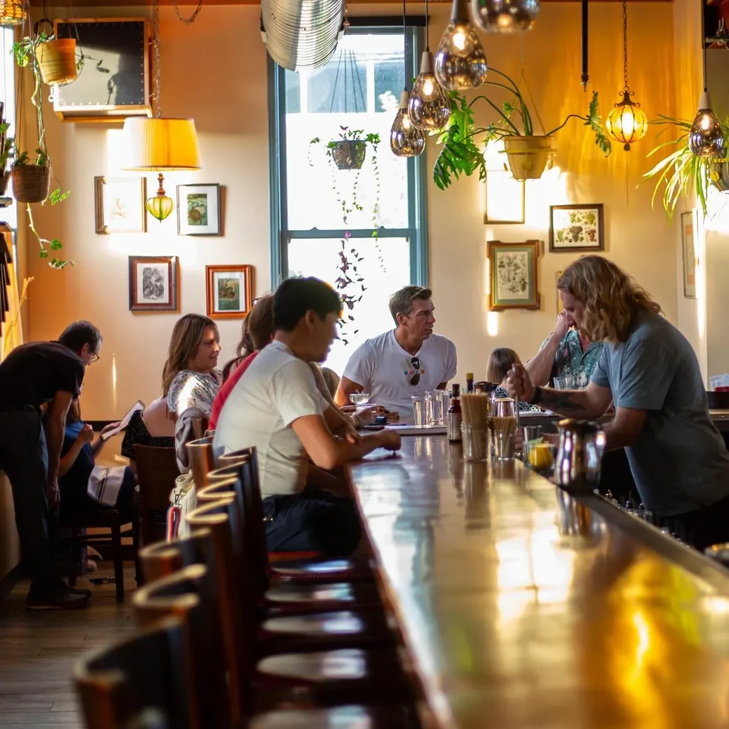 Lively bar interior with patrons at a counter and a bartender.