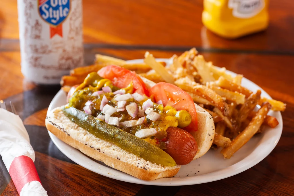 Close-up of a Chicago-style hot dog with fries and a pickle.
