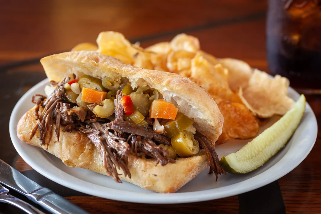 Close-up of shredded meat sandwich, pickled vegetables, chips, and pickle.