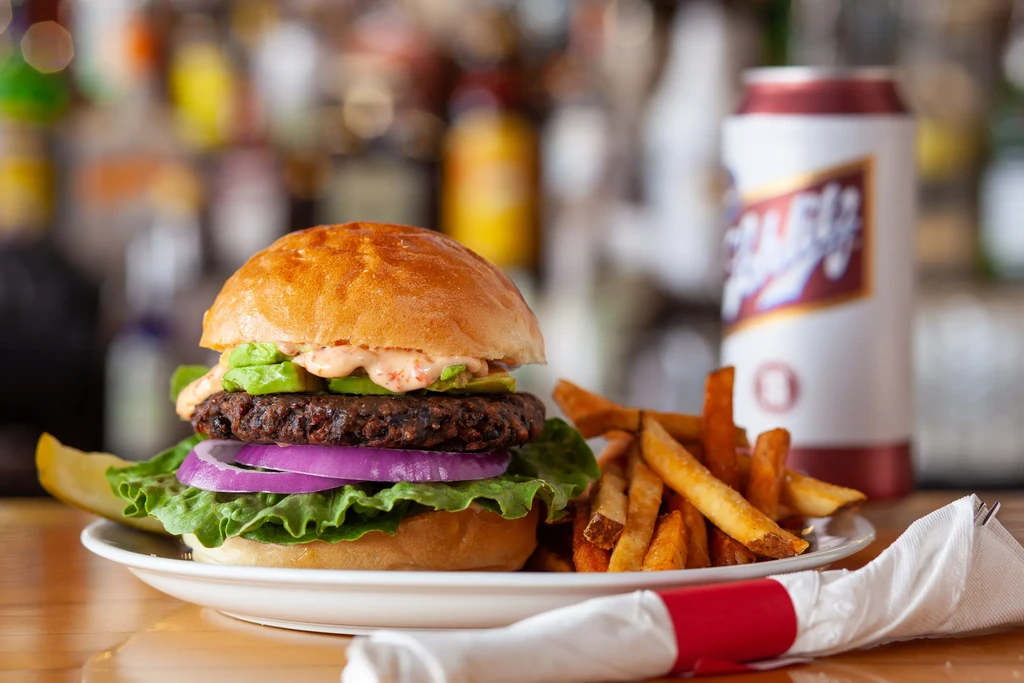 Gourmet plant-based burger with avocado and fries on a wooden table.