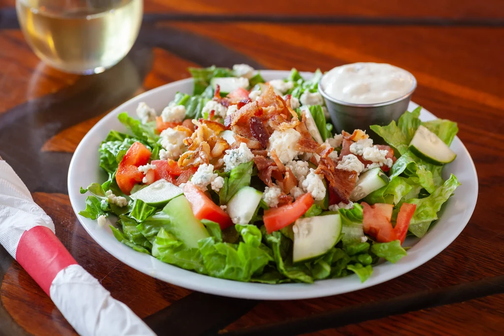 Salad with lettuce, tomatoes, cucumbers, blue cheese, bacon, and dressing.