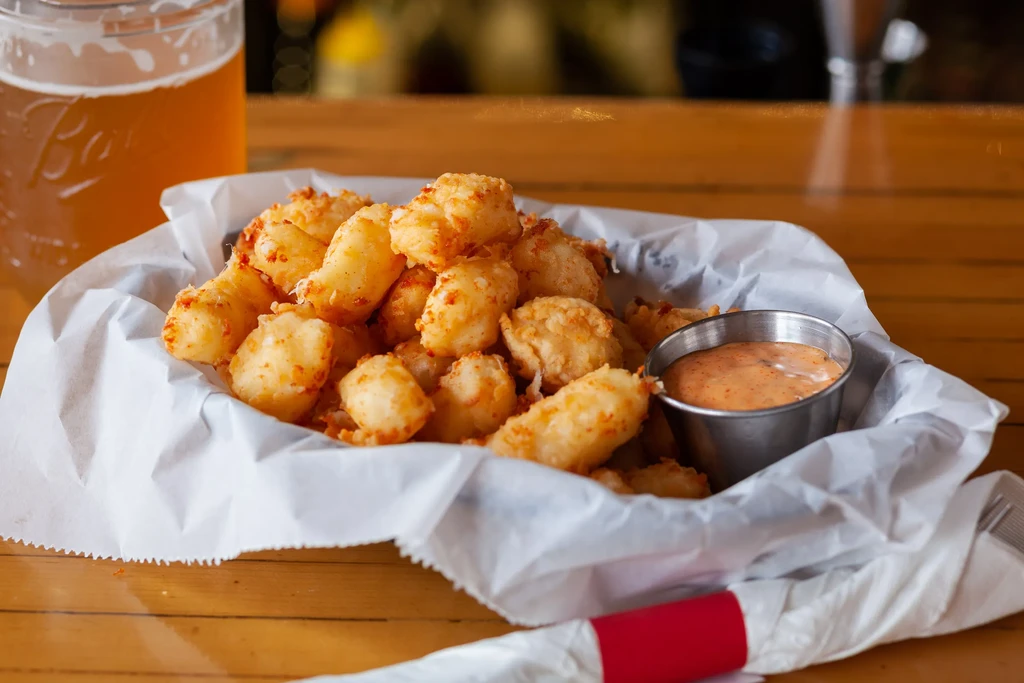 Basket of crispy fried cheese curds with dipping sauce and beer.