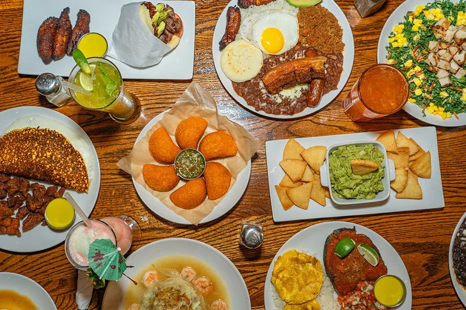 Overhead view of rustic table laden with diverse Latin American dishes and drinks.
