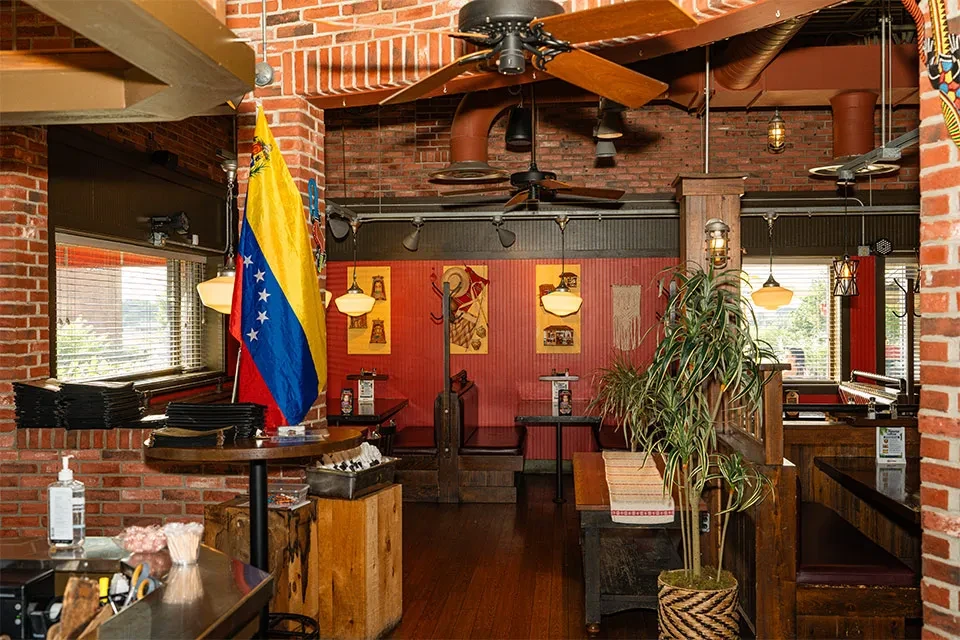 Empty rustic industrial restaurant with red brick walls and Venezuelan flag.
