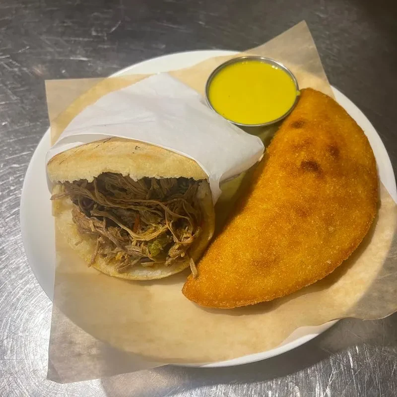 Shredded meat arepa, fried empanada, and yellow sauce on a white plate.
