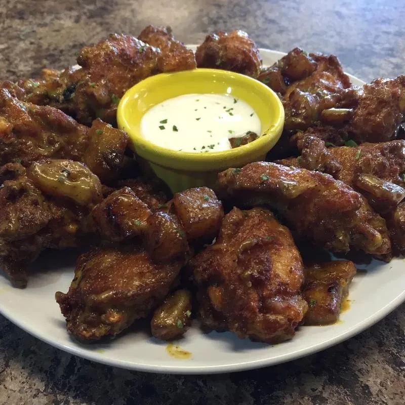 Plate of sauced chicken wings, potato wedges, and herb dip.