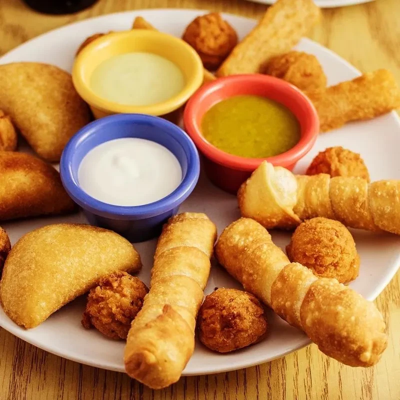 Close-up of fried appetizers with three colorful dipping sauces on a plate.
