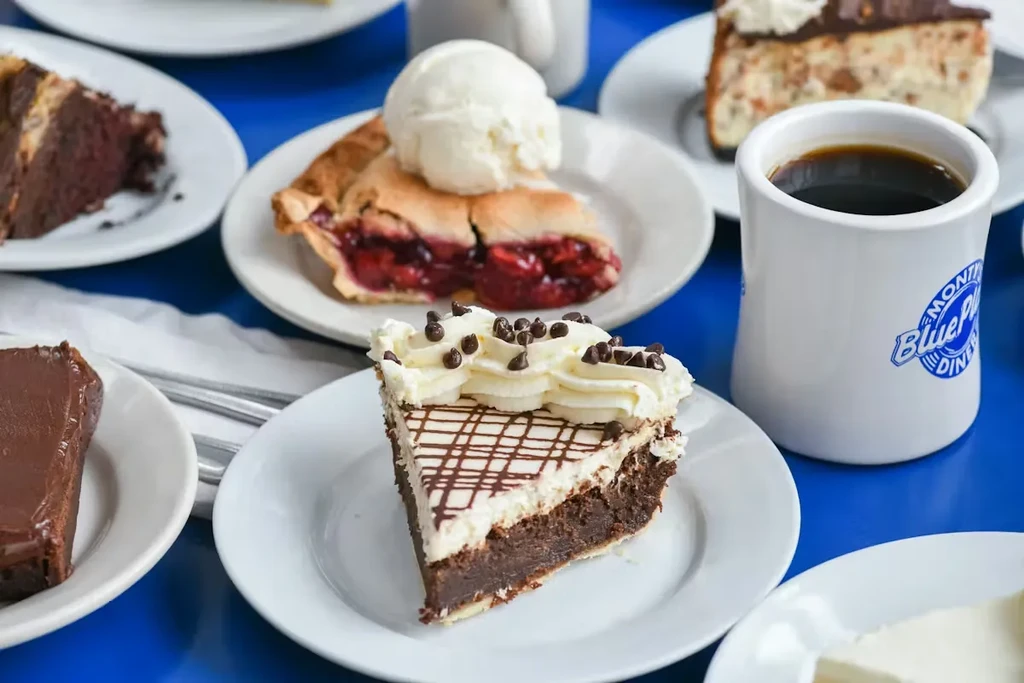 Flat lay of chocolate pie, cherry pie, cakes, and diner coffee mug.