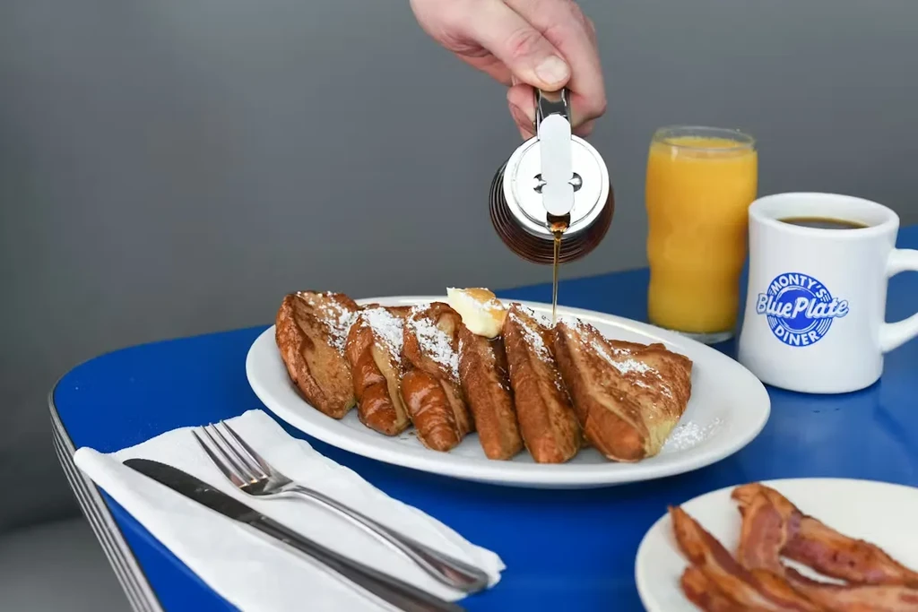 Syrup drizzled on French toast with coffee and juice at a diner.