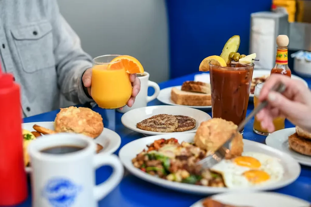 A shared diner breakfast with eggs, sausage, biscuit, and two garnished drinks.