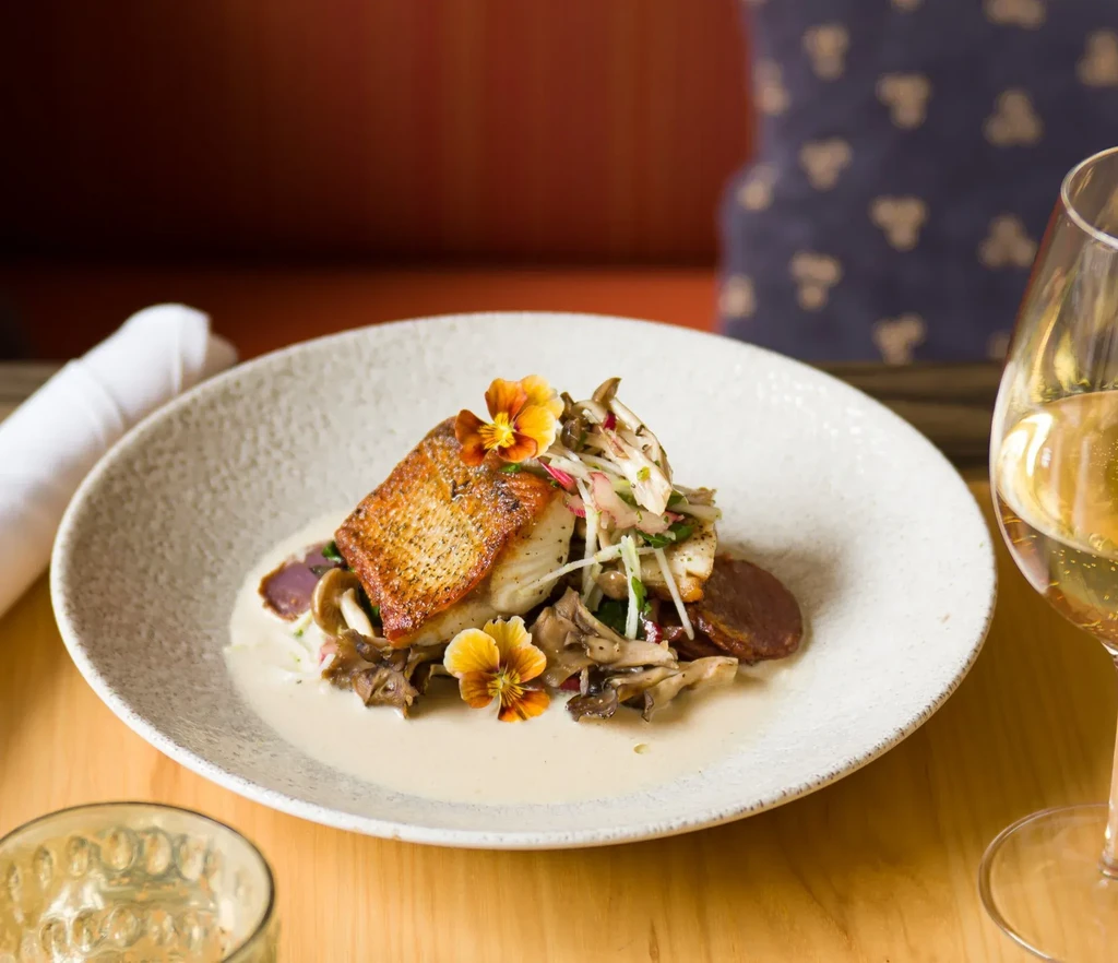 Pan-seared fish, vegetables, edible flowers, sauce, and white wine.