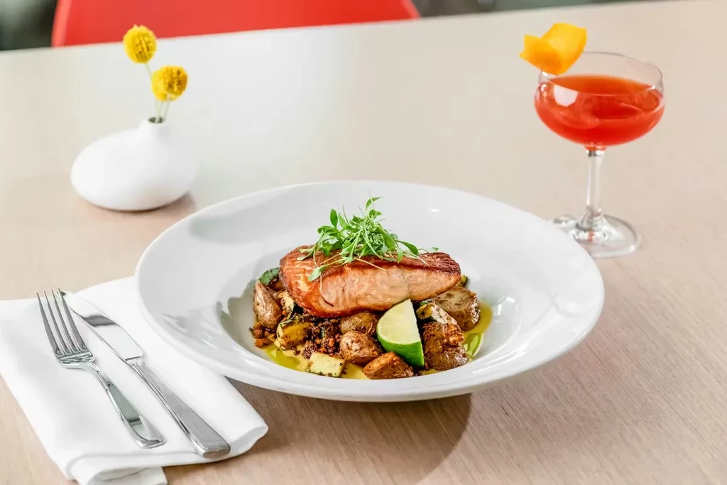 Plated pan-seared salmon with roasted potatoes, microgreens, and cocktail.