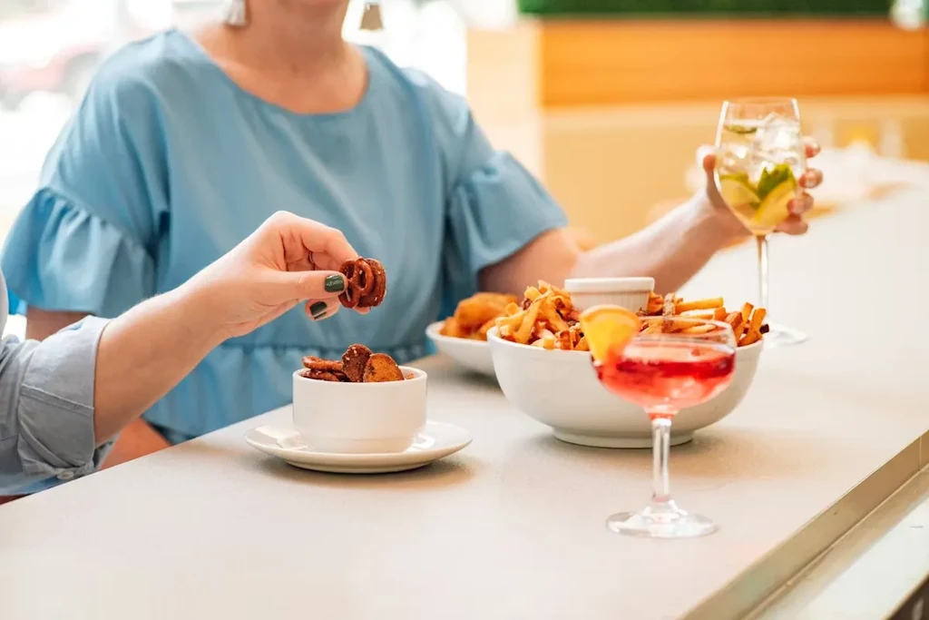 Hands pick spiral snacks and fries with cocktails at a bar.