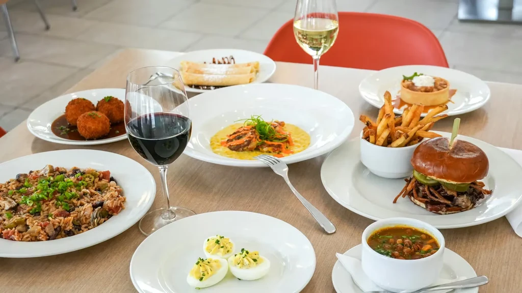 Table spread with diverse food dishes, desserts, red and white wine.