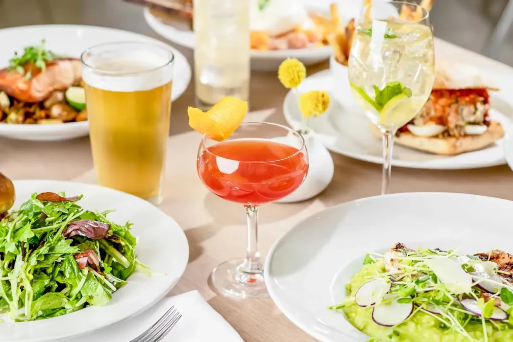 Table with salad, red cocktail, beer, and various restaurant dishes.