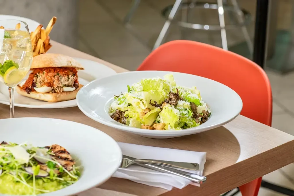 Restaurant table with a Caesar salad, burger, fries, and a refreshing drink.