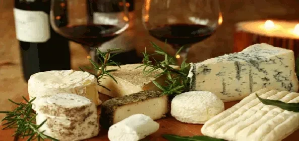 Warm-toned cheese board with various cheeses, rosemary, wine, and candle.