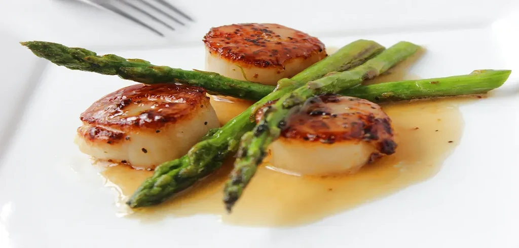 Perfectly seared scallops with asparagus and sauce, elegantly plated.