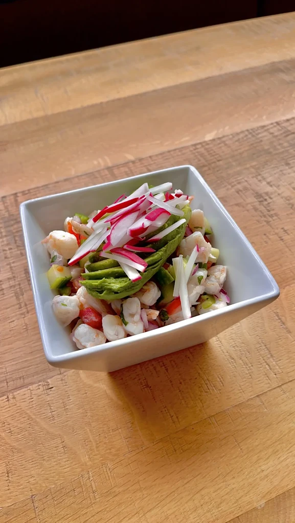Colorful seafood salad with shrimp, radishes, and avocado in white bowl.