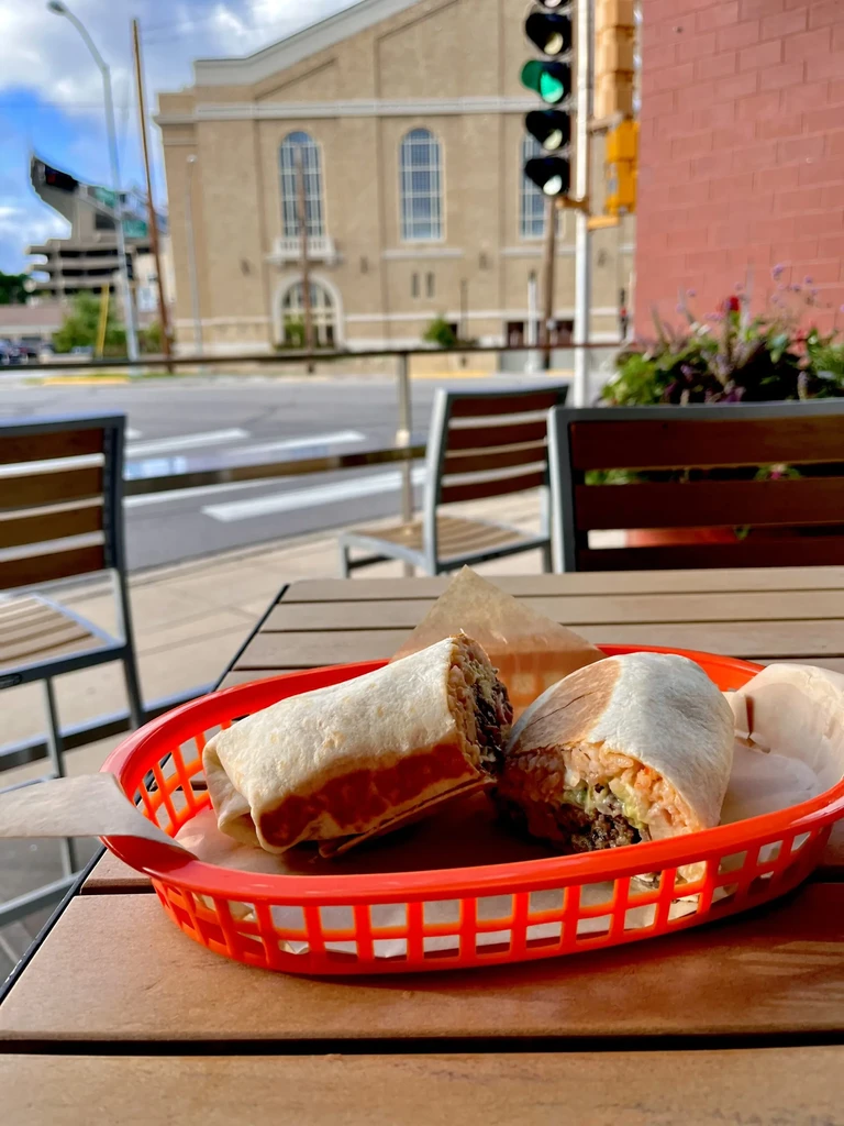 Two burritos, one cut open showing fillings, in outdoor setting.
