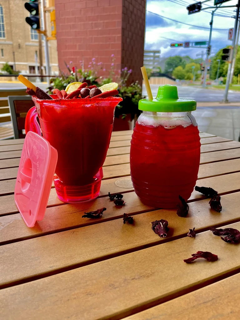 Two vibrant red drinks on a wooden table outdoors with urban background.