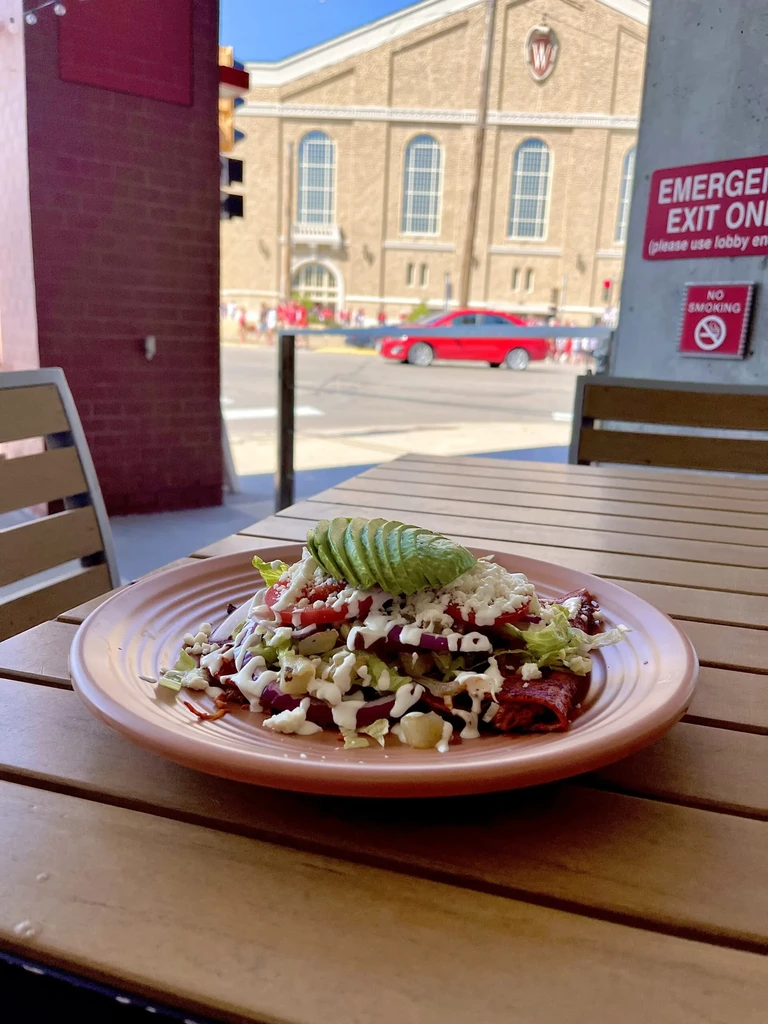 Plate of food with avocado, vegetables, cheese, and sauce on outdoor table.