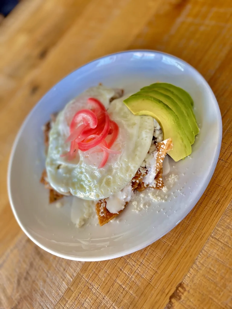 Overhead chilaquiles with fried egg, crema, avocado, and pickled onions.