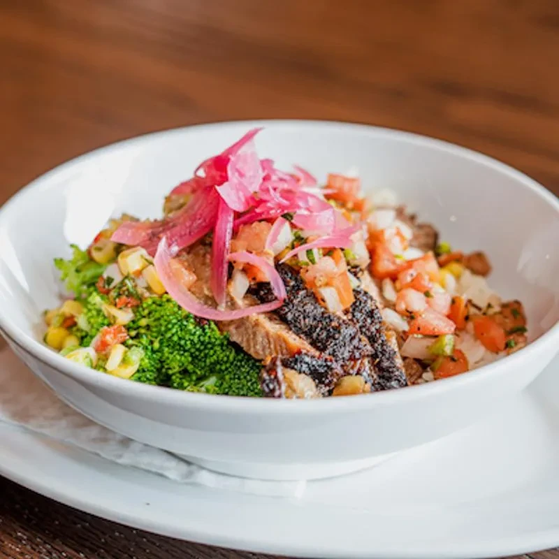Colorful grilled steak bowl with broccoli, corn, and pickled red onions.