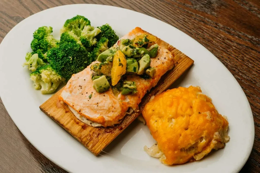 Overhead view of baked salmon with relish, broccoli, and cheesy gratin.